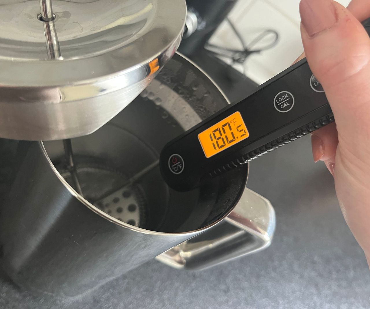 a digital thermometer reading the temperature of water in a stainless steel coffee press. It shows 180F