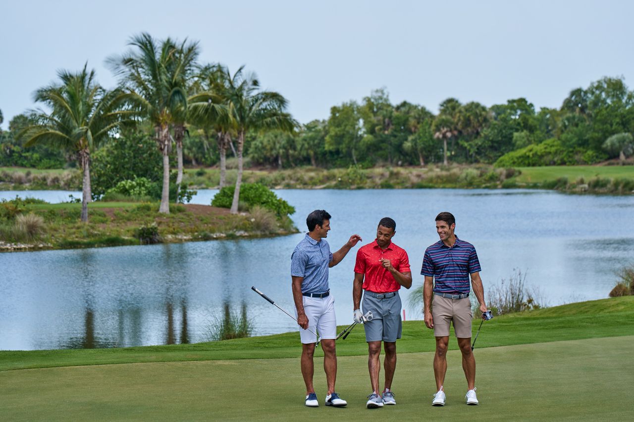 Three male golfers on the green of a golf hole next to a lake