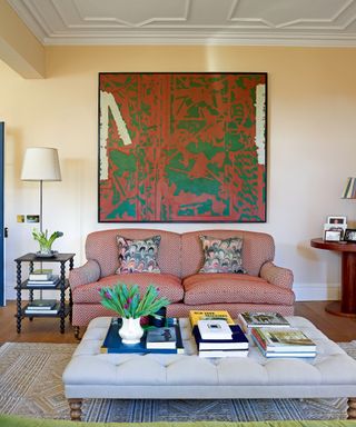 neutral living room with red zig zag sofa, pink and green artwork, and off white buttoned ottoman