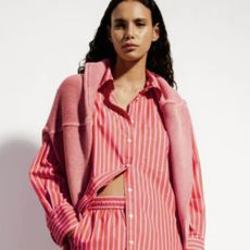 Young woman wearing pink striped co-ord with pink fleece, staring at camera.