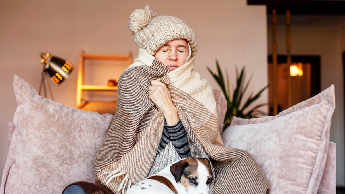 Woman wrapped in blanket and wooly hat on sofa