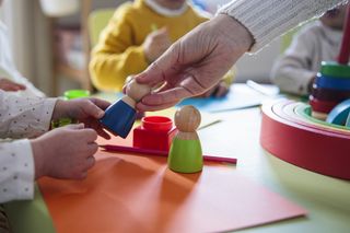 Close up of adult and child hands playing with wooden toys on a nursery table