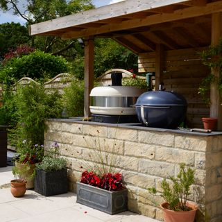 an outdoor kitchen with a Gozney pizza oven and a kettle bbq