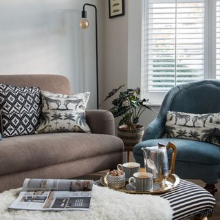 A small living room with a taupe sofa and a blue accent chair paired with a striped ottoman for a coffee table