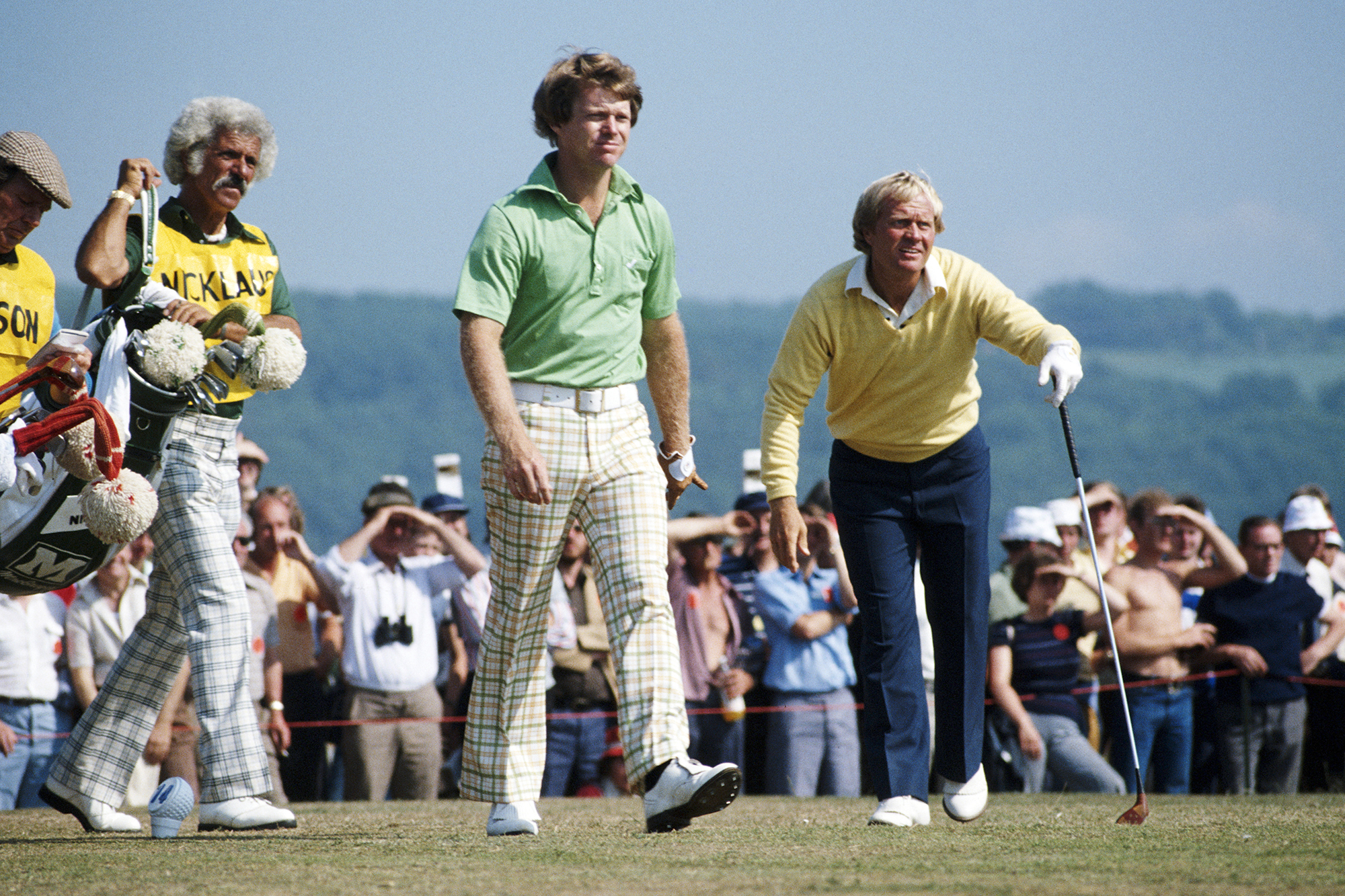Tom Watson and Jack Nicklaus teeing off together, with their caddies carrying their bags beside them
