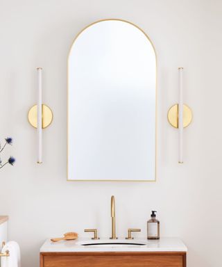 Gold bathroom mirror with statement wall sconces and a wood vanity