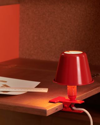 Red clip-on metal lamp attached to wooden desk edge