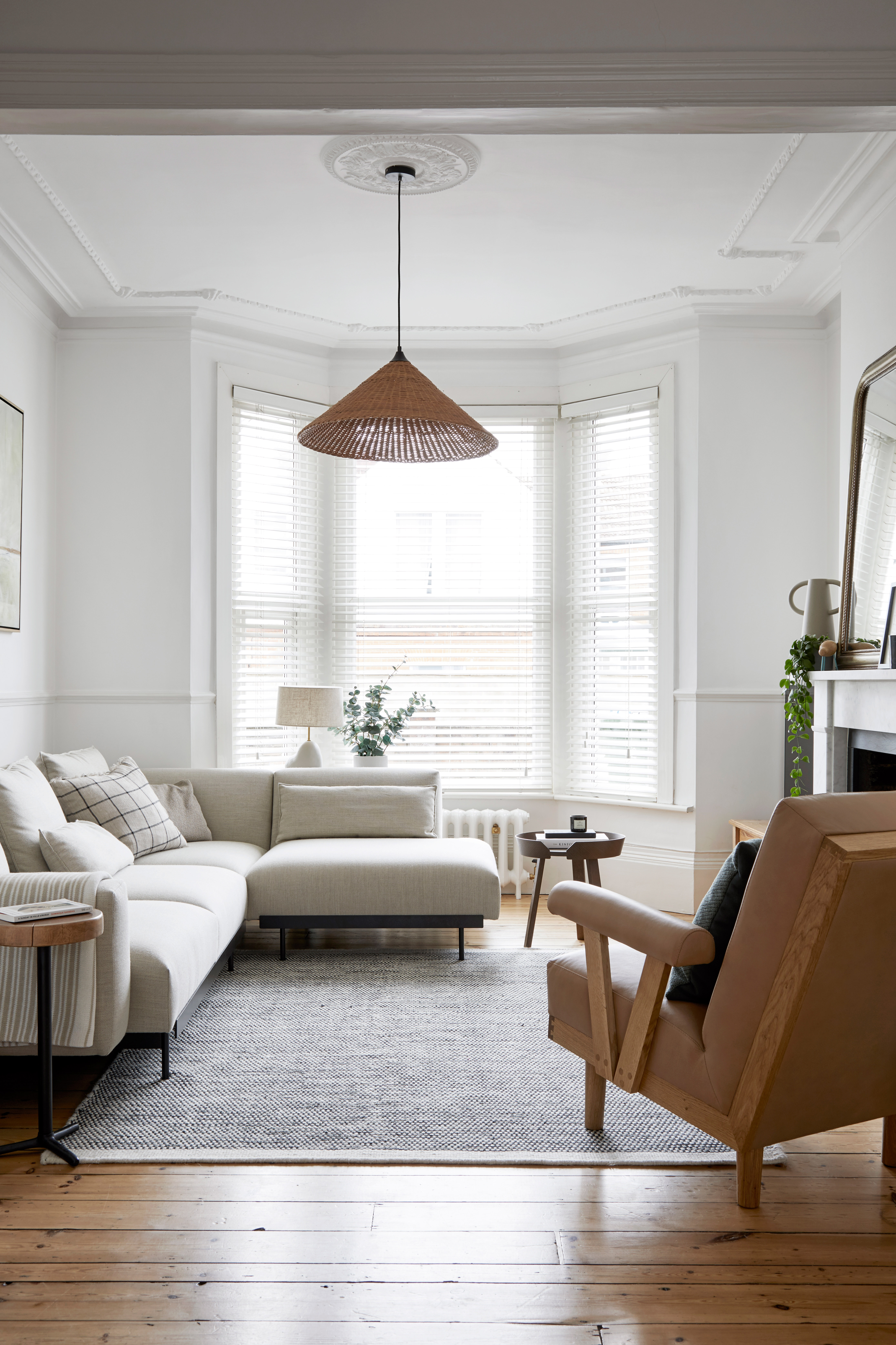 Neutral Scandi-style living room with white walls and a bay window. There is a white sectional sofa and a gray area rug over hardwood floors.
