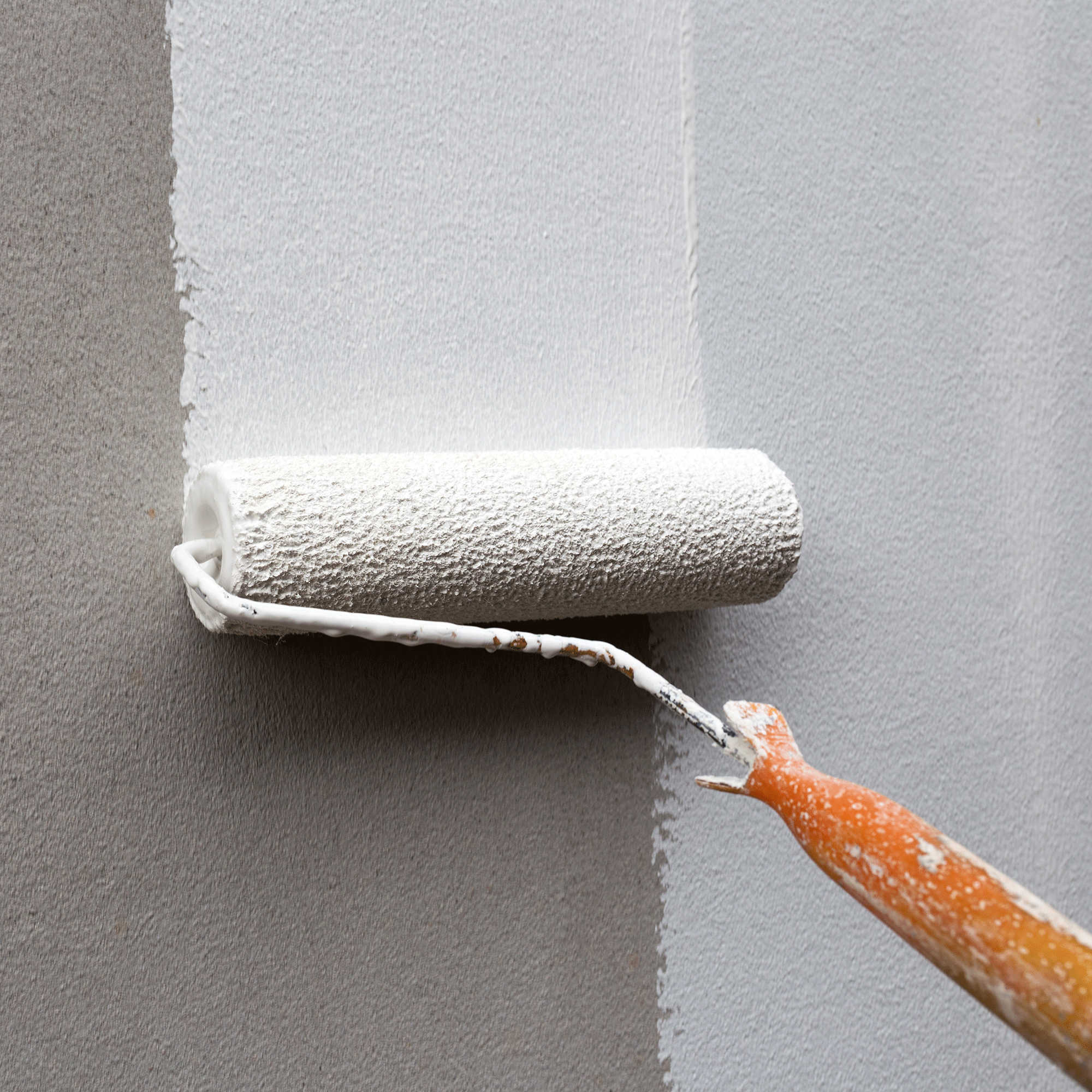 Wooden handled paint rolled with white paint on a wall