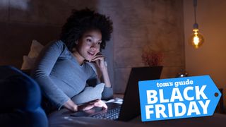 Woman lying in bed looking at laptop with Tom's Guide Black Friday badge overlaid