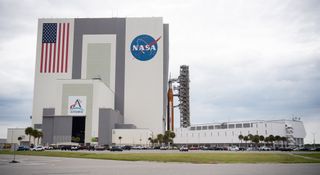 a huge orange rocket being wheeled into a massive white building