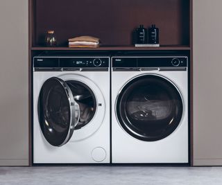 Two tumble dryers, one is open and both contain laundry