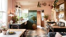 Peach kitchen with checkered floor and pot hanging rail. Green cabinets and butler sink on left, with wooden counters on the rights and mounted shelving