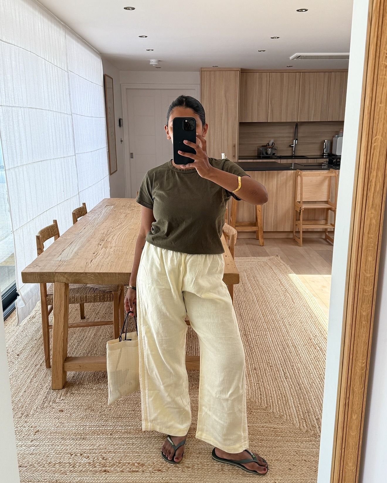 A woman wearing green flip flops, yellow linen trousers, and a green crewneck.