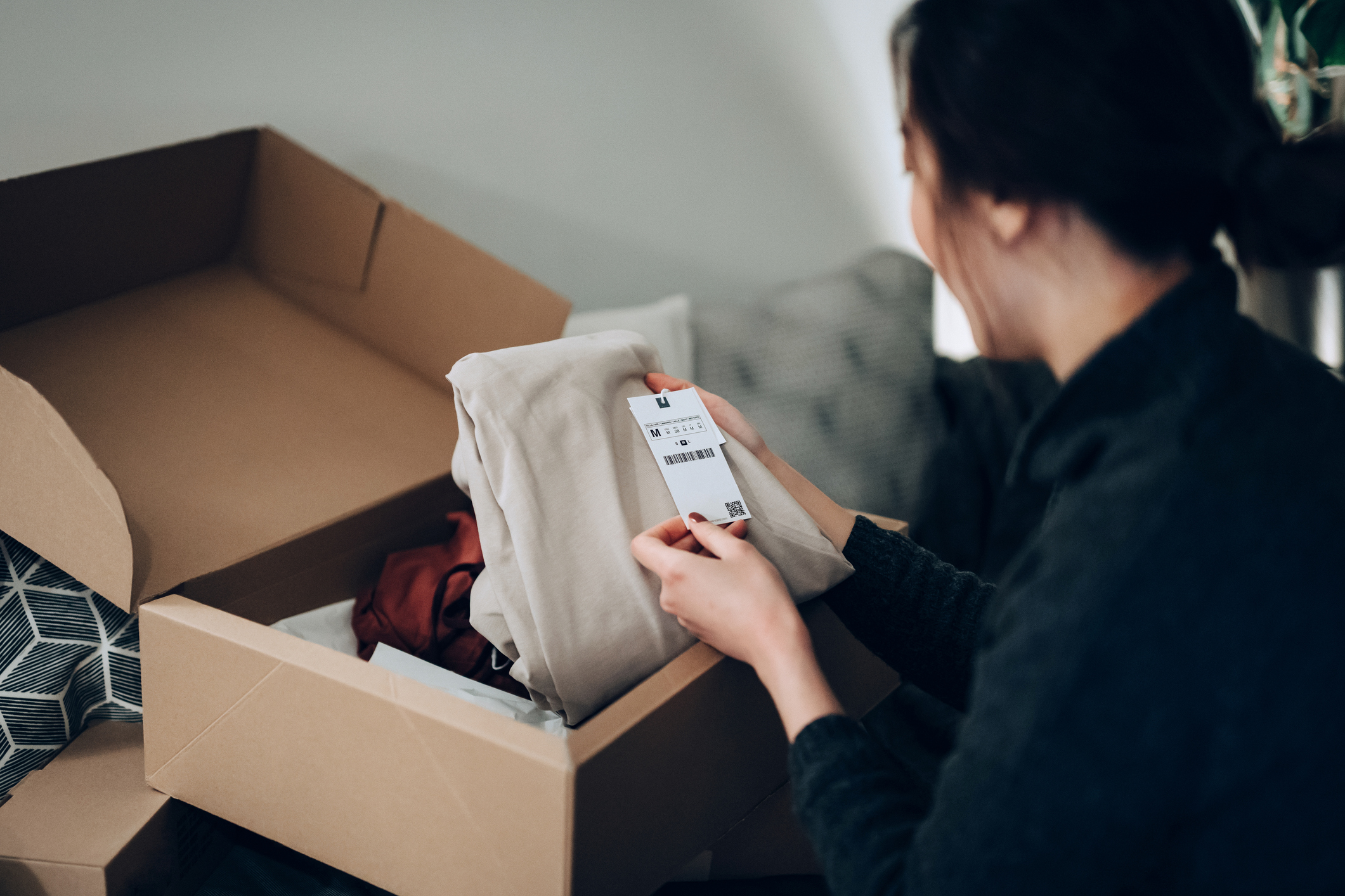 A woman checking a clothing label with a box on her lap from a delivery.