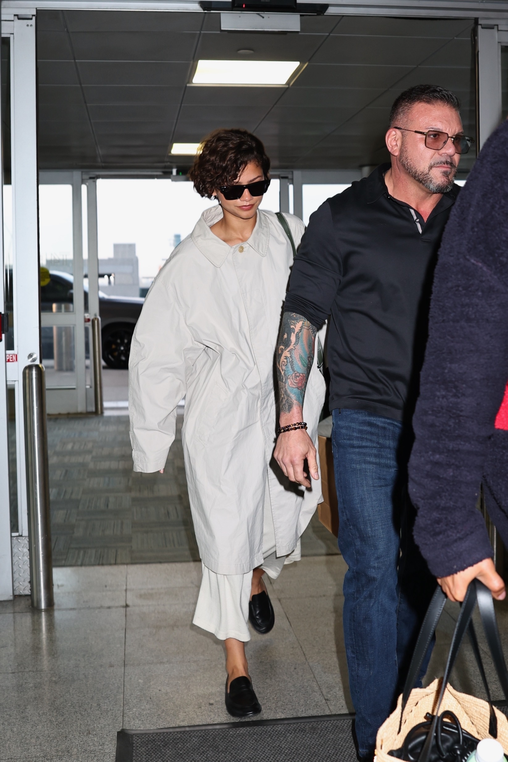 Zendaya heads to the airport in a white The Row trench coat, a white skirt, and black loafers, tapping into two Spring 2026 It-Girl trends