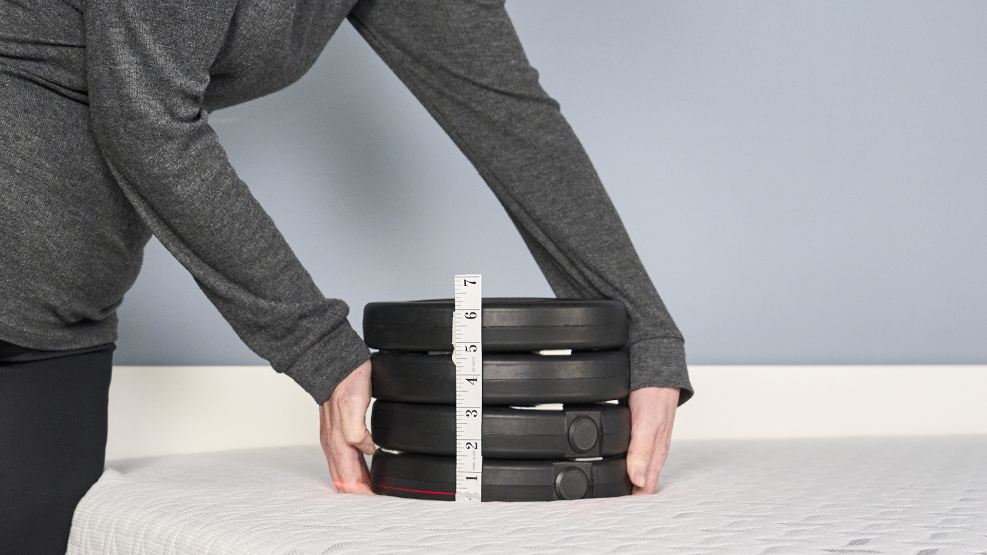 A close up of sleep writer Ruth Jones placing a stack of weight (consisting of four 2.5kg weights) on the sleeping area of the Nectar Premier Memory Foam Mattress. A tape measure is attached to the side of the weights and a laser line can be seen hitting the bottom of the tape measure, indicating just how far into the materials the weights have sank.