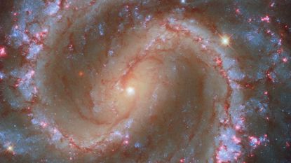 A glowing spiral galaxy with pink and purple and yellow gas swirls around small dots of young stars in space