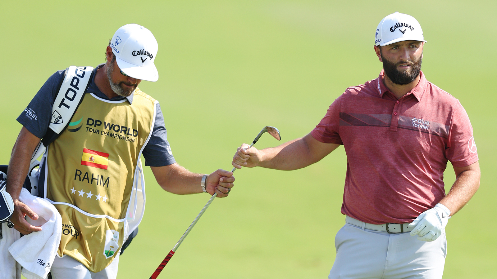 Jon Rahm's caddie hands him a club