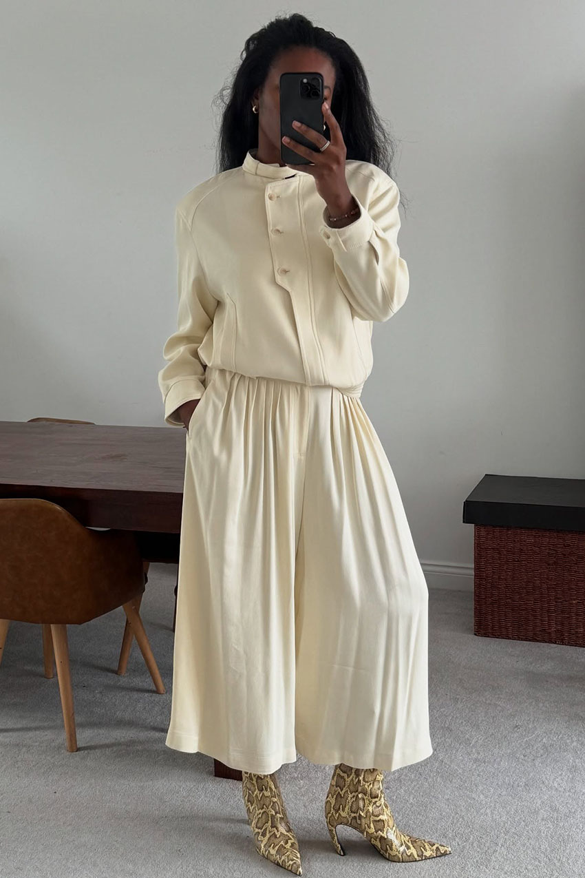 A woman wearing a cream color jacket and loose pants with snakeskin boots