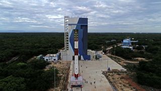 a white and red Indian PSLV rocket is wheeled toward a large blue building