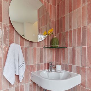 Pink bathroom tiles in a corner with a corner sink and round mirror