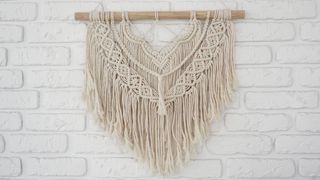 A boho fabric wall hanging against a white brick wall.