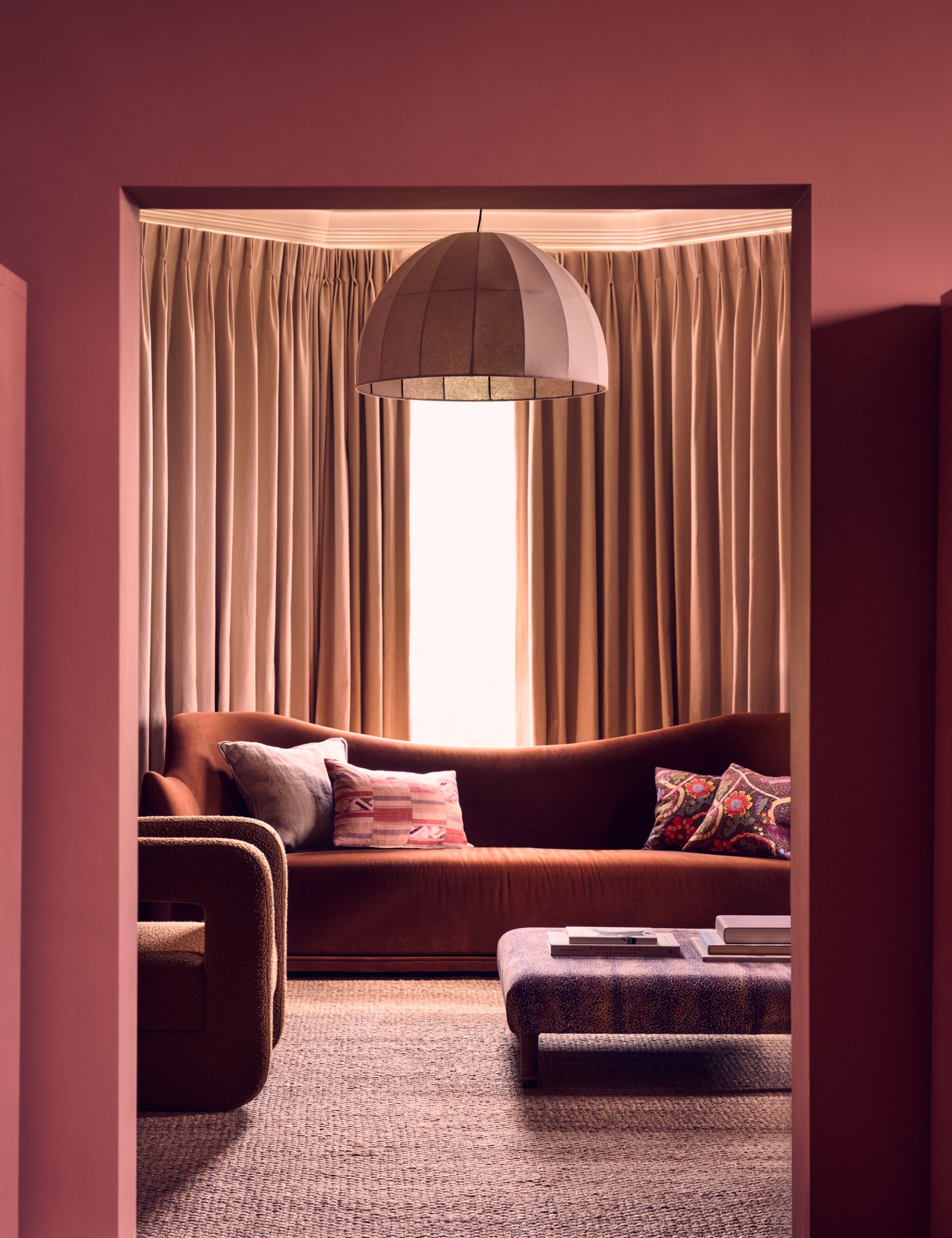 Deep clay living room with curved rust colored sofa, beige curtains and texture rug