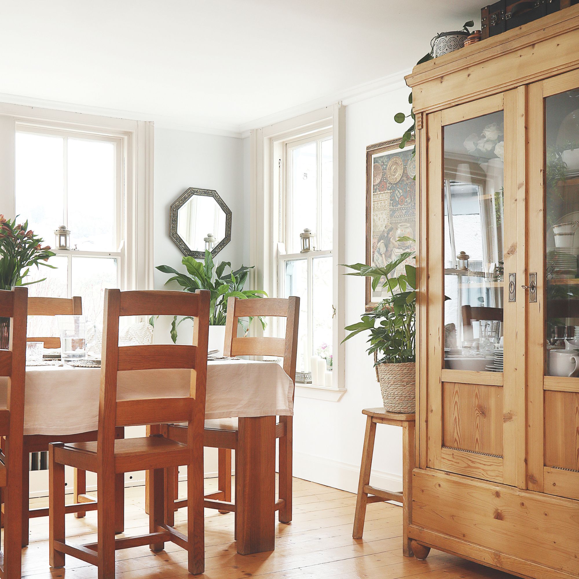 A bright dining room with a rectangular wooden table and a matching chairs and a glass-door display cabinet