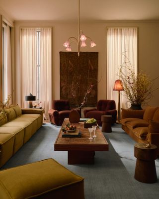 Living room with magnolia walls, muted blue rug, wood coffee table, yellow sofa and burgundy armchairs