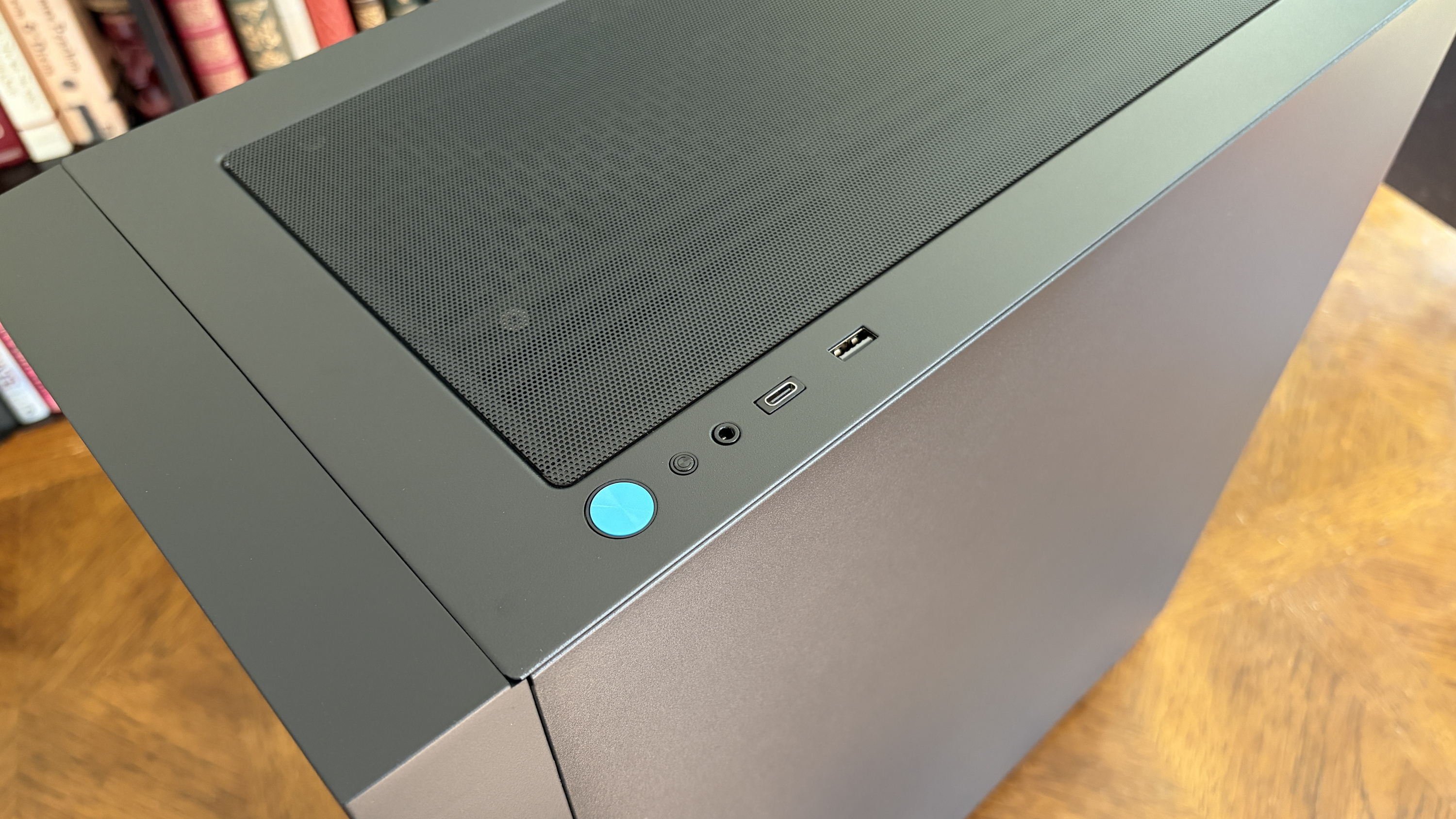 A sleek black MG-1 MK.II PC tower with a vented top panel, USB ports, and a blue power button sits on a wooden surface, exuding a modern, minimalist design.
