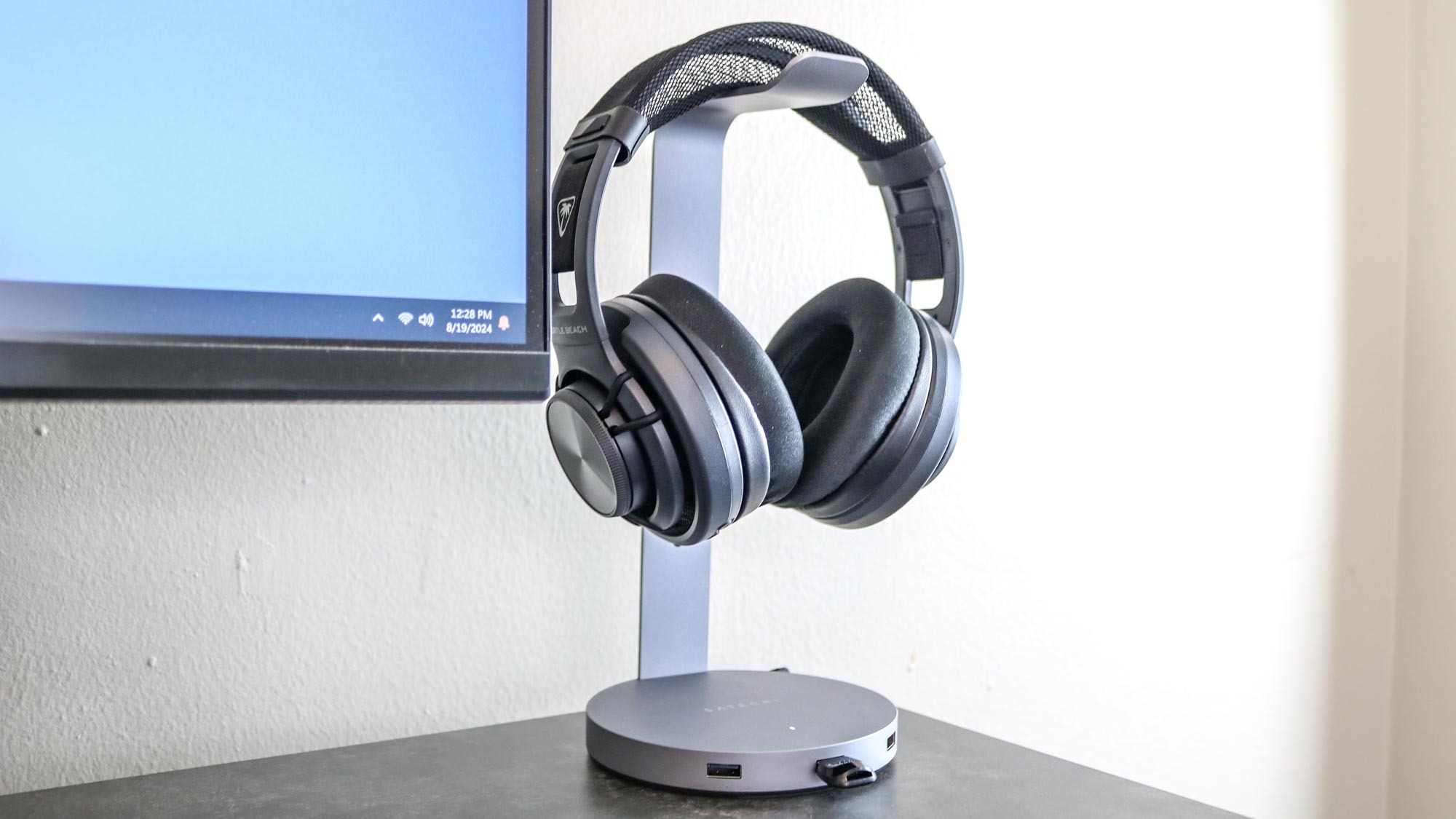 The Satechi aluminum USB headphone stand on a desk with a pair of headphones hanging from it