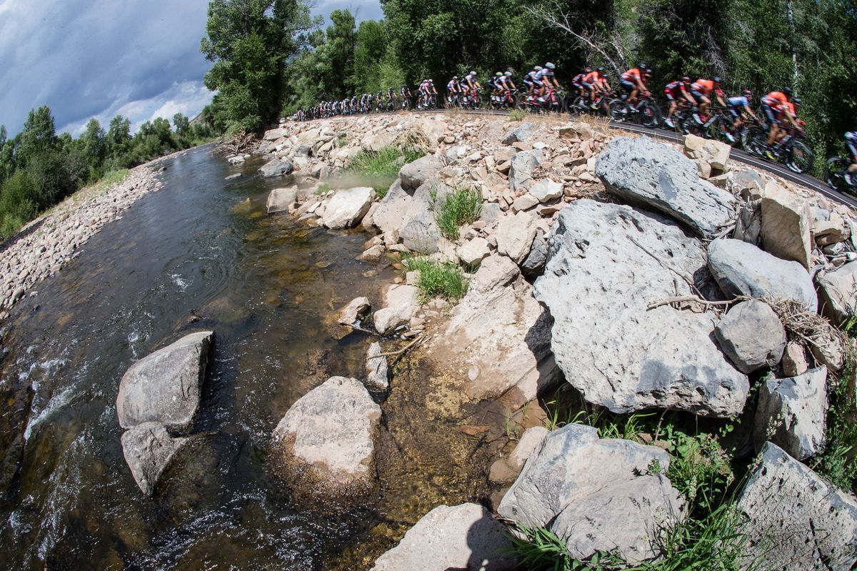 Riders pass by a river on the way to the climb