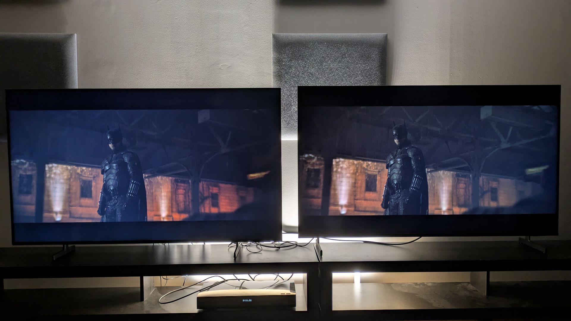 Samsung M80H (left) vs Samsung QN80H (right) showing Batman from The Batman on screen. The QN80H has stronger contrast, but both TVs show screen uniformity issues