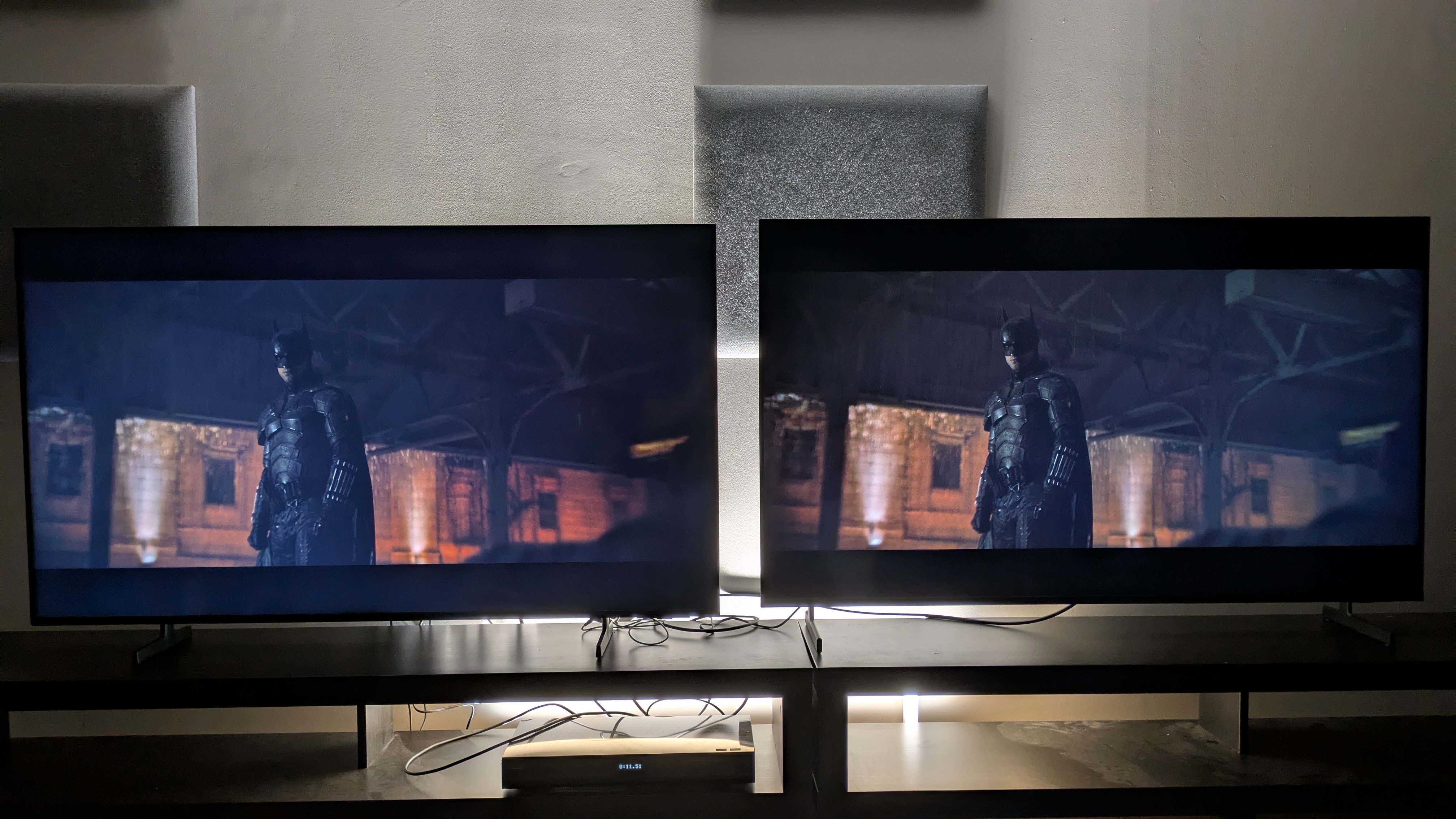 Samsung M80H (left) vs Samsung QN80H (right) showing Batman from The Batman on screen. The QN80H has stronger contrast, but both TVs show screen uniformity issues