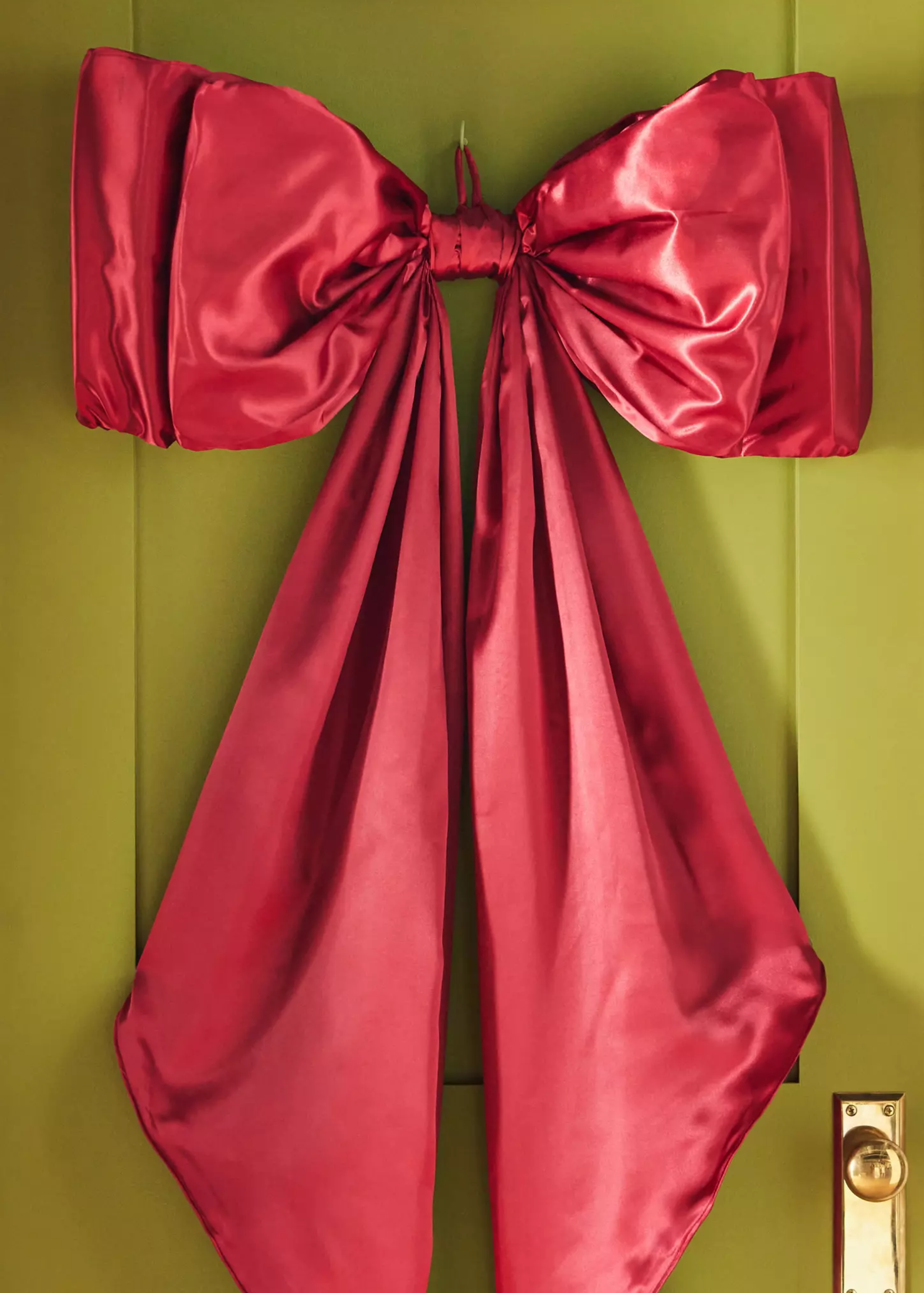 Anthropologie red Satin Bow Tree Topper used as a wreath on a green door with a gold handle