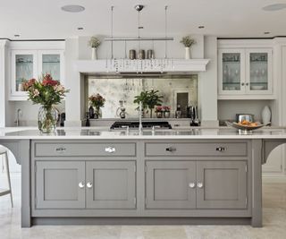 A grey kitchen with white walls and large kitchen island. An antique mirror splashback behind the stove.