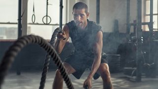 Man performing battle ropes holding them in both hands and creating waves during battle rope workout