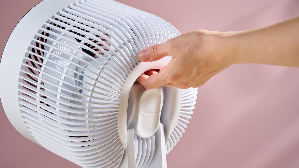 A woman is about to lift the fan by the integrated carry handle.