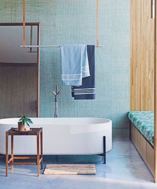 A blue tiled bathroom with a long white back and two blue towels hanging from a roof hanger