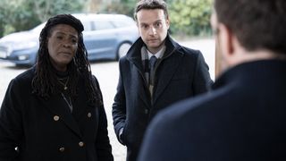 Sharon D Clarke in a black coat as Ellis and Andrew Gower in a dark coat as Harper at a doorway talking to someone in Ellis.