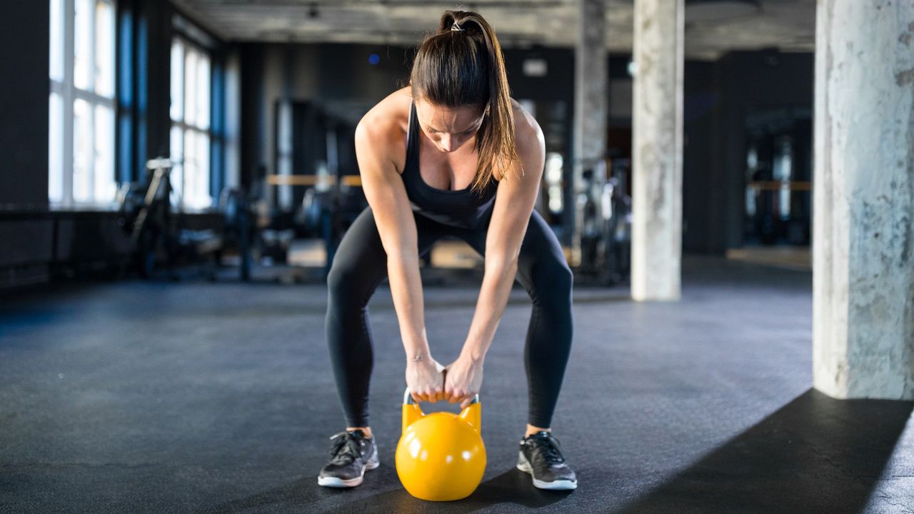 Woman bending down to pick up a kettlebell during kettlebell challenge