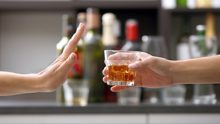 Woman puts out hand to reject glass of alcohol