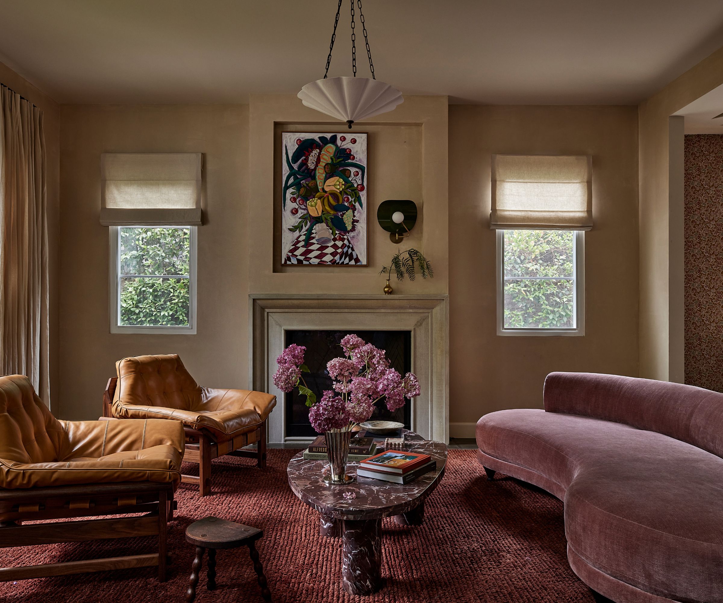 A modern living room with neutral walls, a fireplace, a plum-colored rug, and a mauve curved sofa.