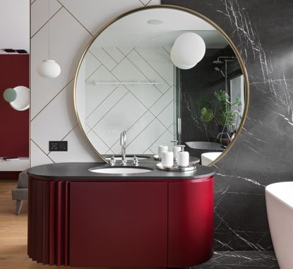 A small bathroom with a round mirror and a red vanity