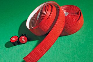 two rolls of lizard skin dsp bar tape in red sat on a green background with two bar ends to match