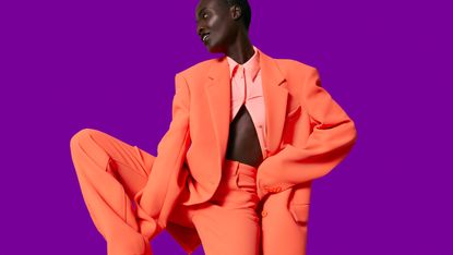 A model wears a neon orange oversized jacket and straight pants in neoprene-like polyester.