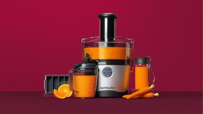 Nutribullet Pro Juicer with oranges and carrots on claret / deep red background