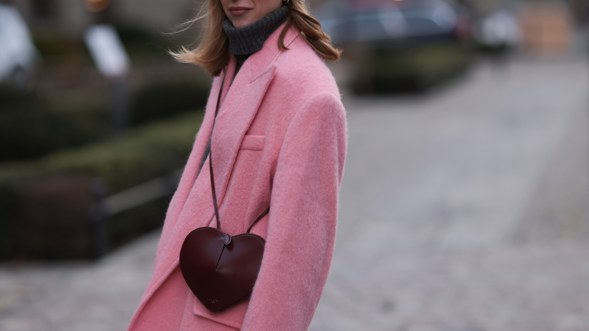 a woman wearing a pink coat with a burgundy heart purse in street style