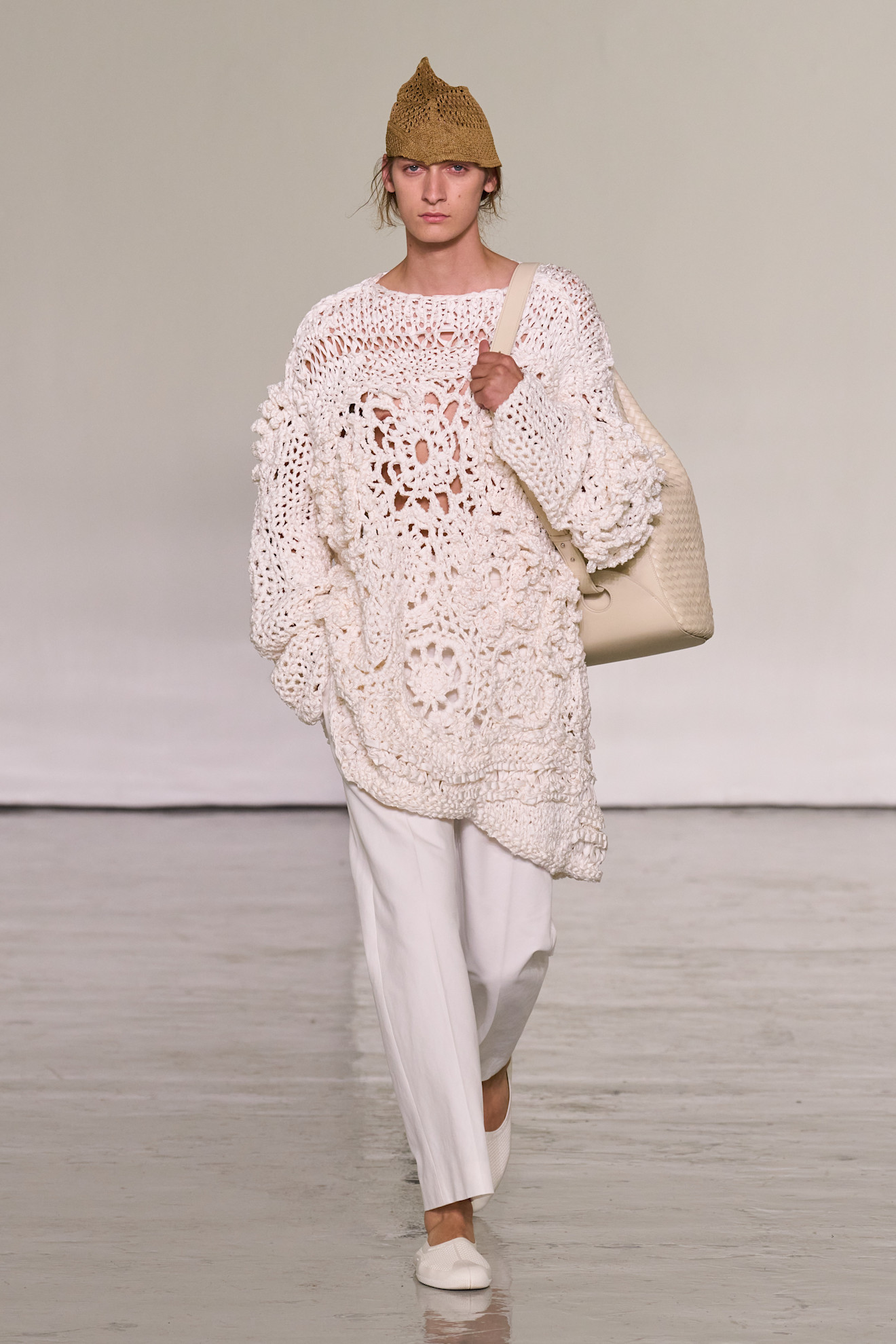 A model walks the runway at Bottega Veneta's spring/summer 2027 Milan Fashion Week show wearing a hand-knit crochet sweater with white poplin pants and white flats.
